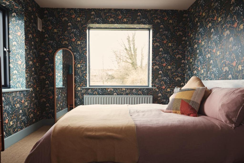 una camera da letto con un letto con carta da parati floreale e una finestra di Contemporary yet cosy and characterful home in rural village setting a Kilfenora