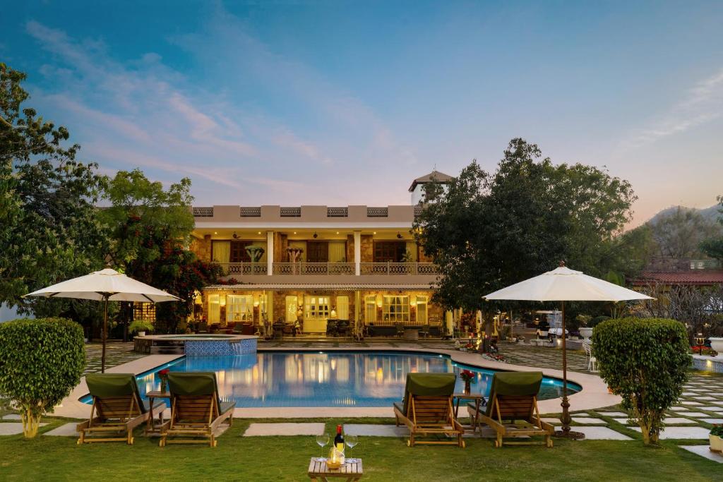a hotel with a swimming pool and chairs and umbrellas at Vatsalya Vihar - A Luxury Pool Villas Resort in Udaipur