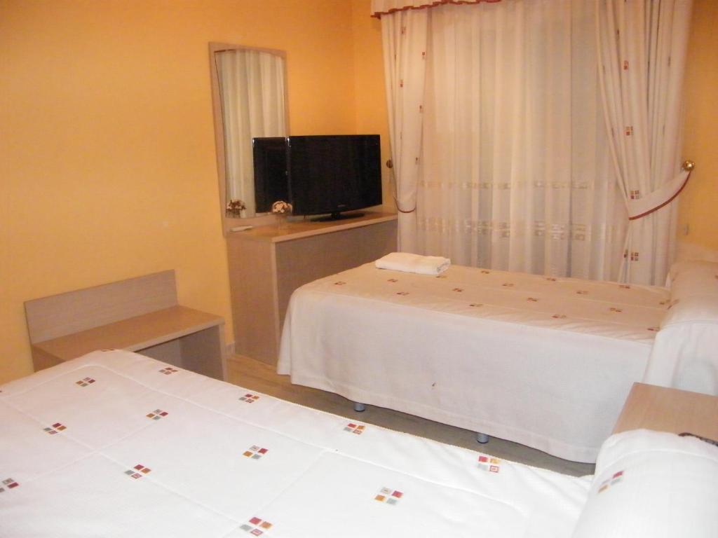 a bedroom with two beds and a tv and a window at Hostal Dulcinea in Esquivias