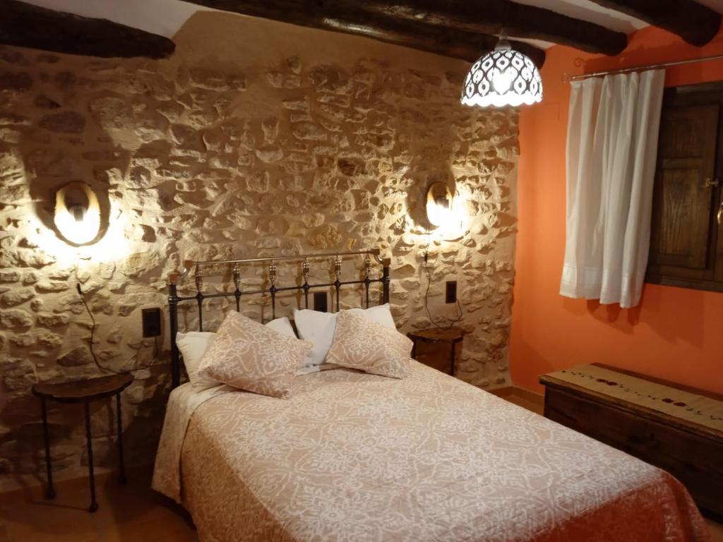 1 dormitorio con cama y pared de piedra en CASA RURAL LES ROQUETES, en Ráfales