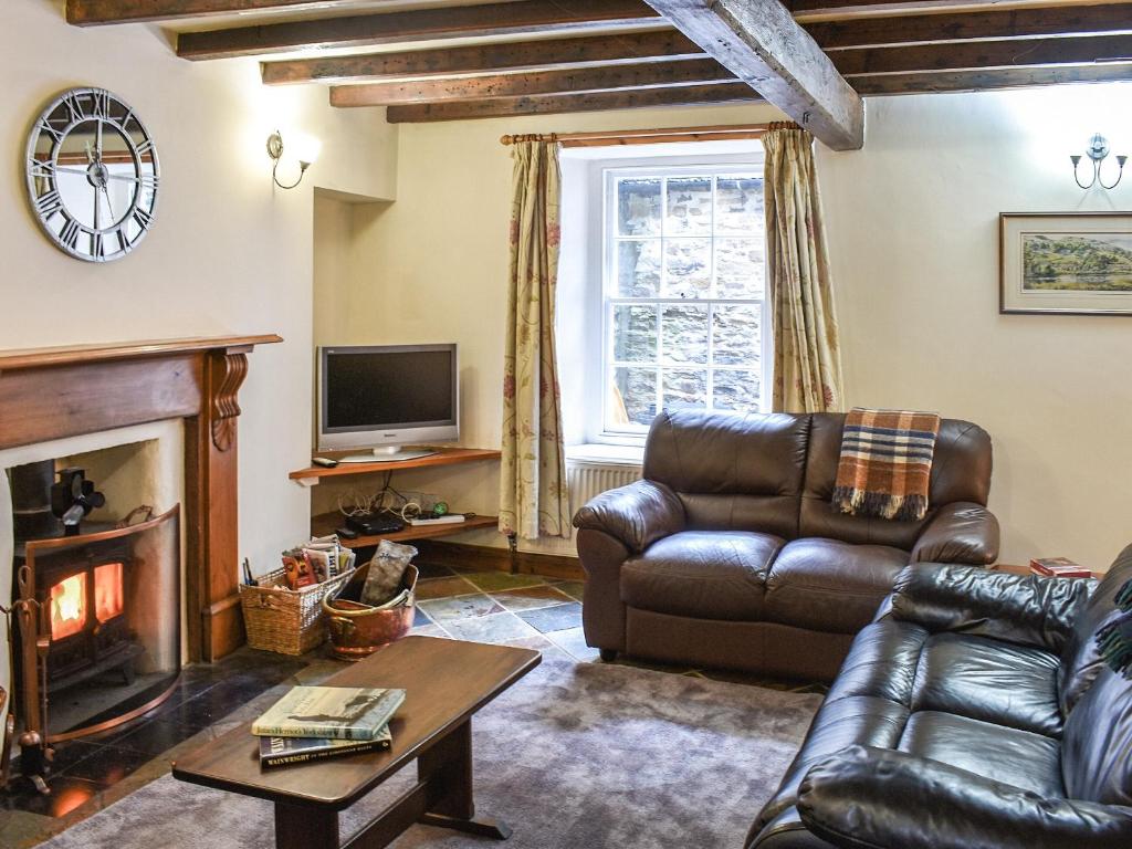 a living room with a leather couch and a fireplace at Stable Cottage in Askrigg