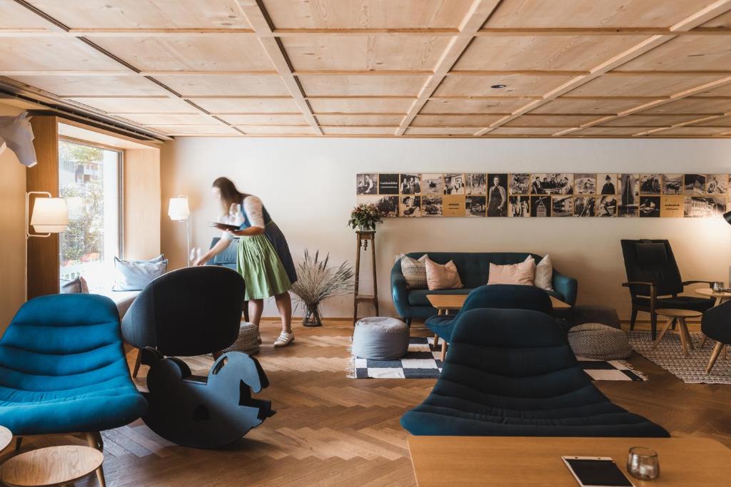 a woman standing in a living room with blue chairs at Hotel Rössle in Au im Bregenzerwald