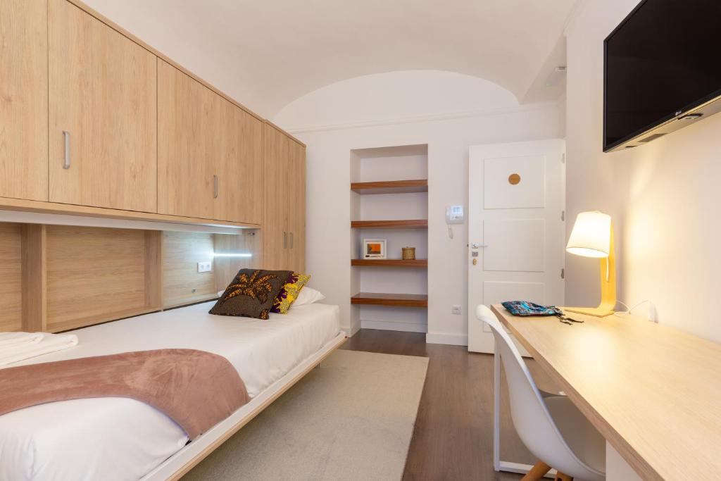 een slaapkamer met een bed en een bureau met een televisie bij Evora Spot Rooms in Évora