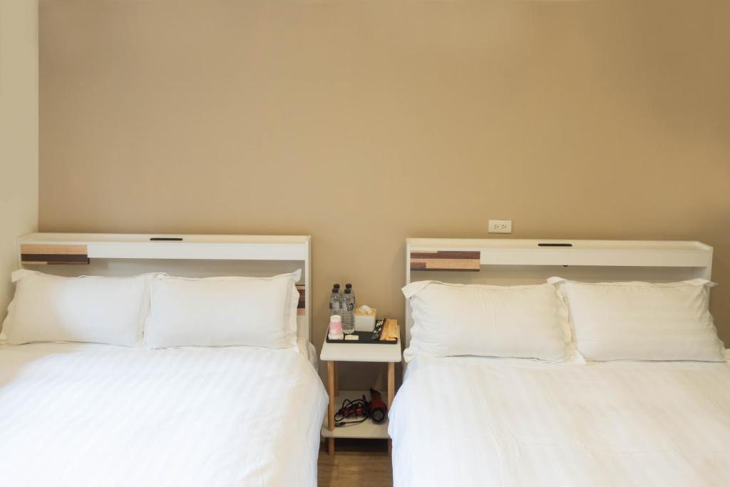 two beds in a bedroom with white sheets and pillows at Cen Pin B&amp;B in Jiufen