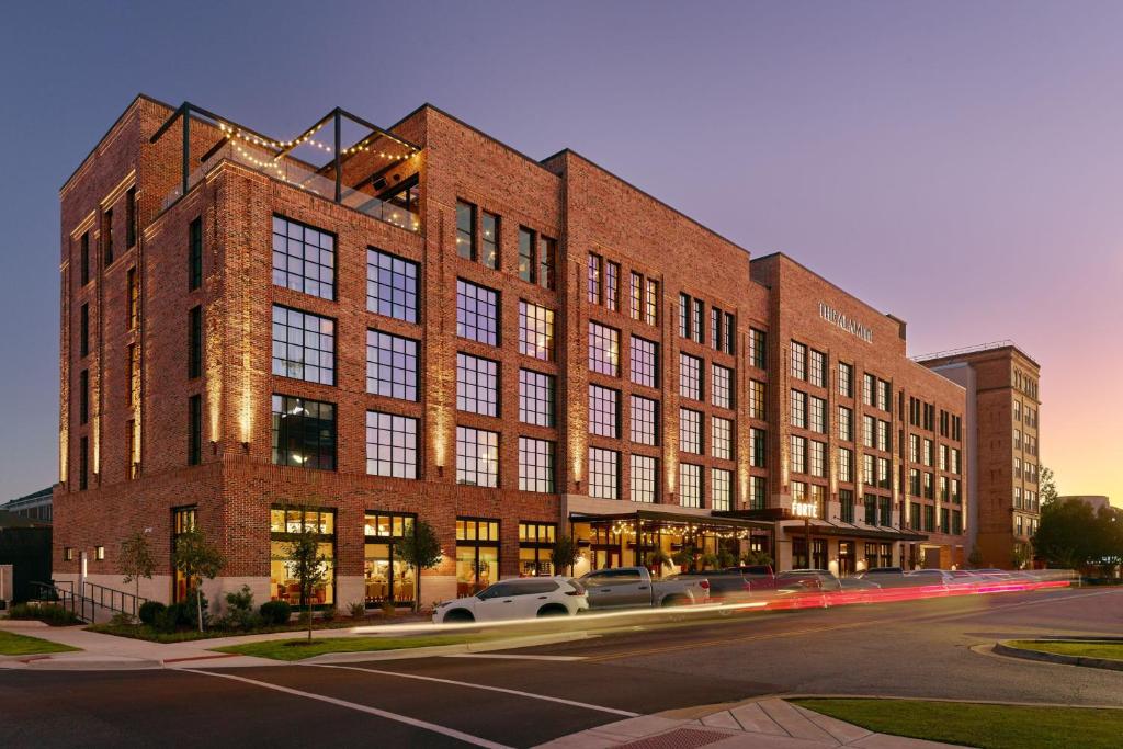 um grande edifício de tijolos com carros estacionados em frente em The Alamite, Tuscaloosa, a Tribute Portfolio Hotel em Tuscaloosa