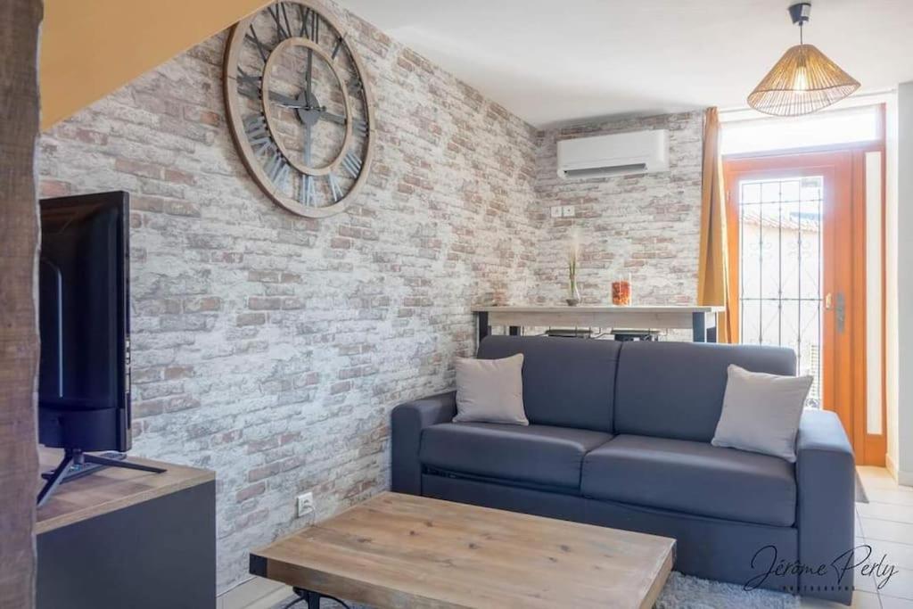 a living room with a blue couch and a clock on a brick wall at Appartement tout confort in Fay-aux-Loges