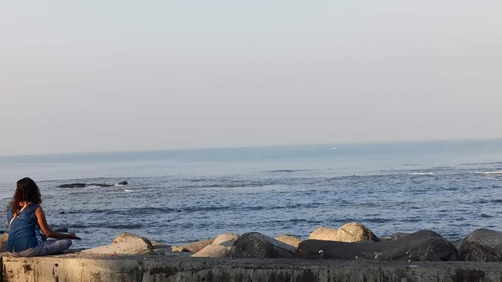 una mujer sentada en las rocas cerca del agua en SEAVIEW Room Bandra W Bandstand Nr Taj WOMEN ONLY, en Bombay