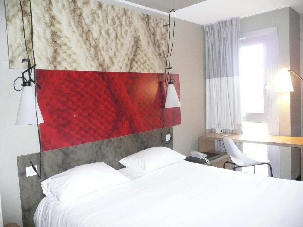 une chambre avec un lit blanc et un mur rouge dans l'établissement ibis Saint Brieuc Yffiniac, à Yffiniac