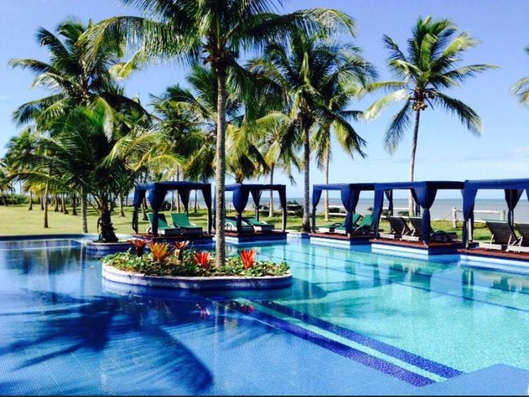 uma piscina de resort com palmeiras e o oceano em Villa Oberoi pé na areia alto luxo em Santo André