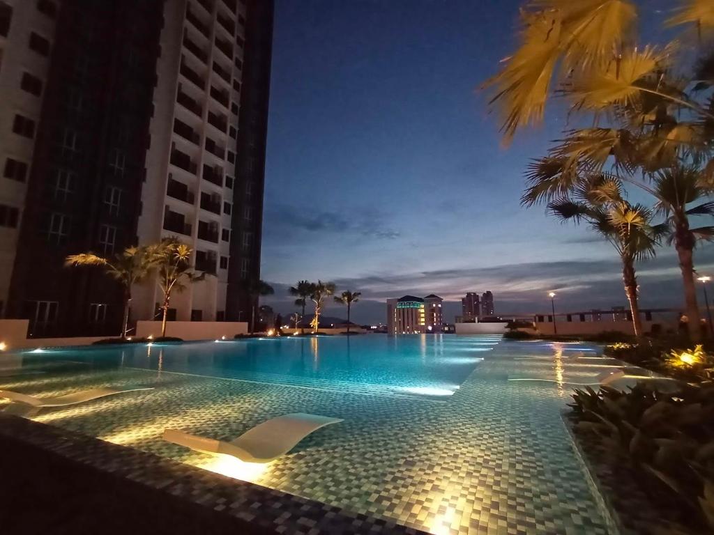 uma piscina à noite com palmeiras e edifícios em Metropol Serviced Apartment em Bukit Mertajam
