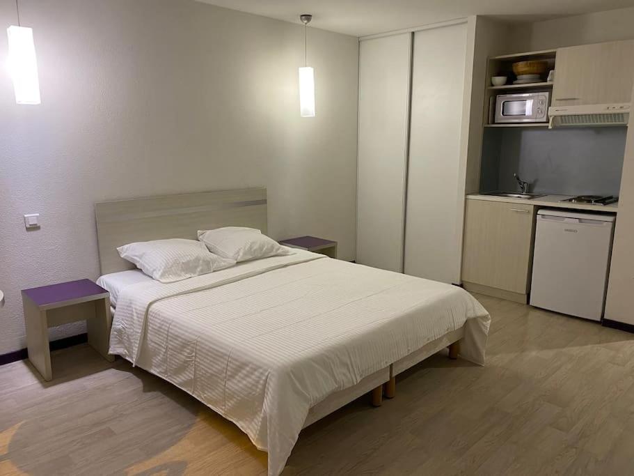 a bedroom with a white bed and a kitchen at Appartement Avenue de la Gare in Lourdes