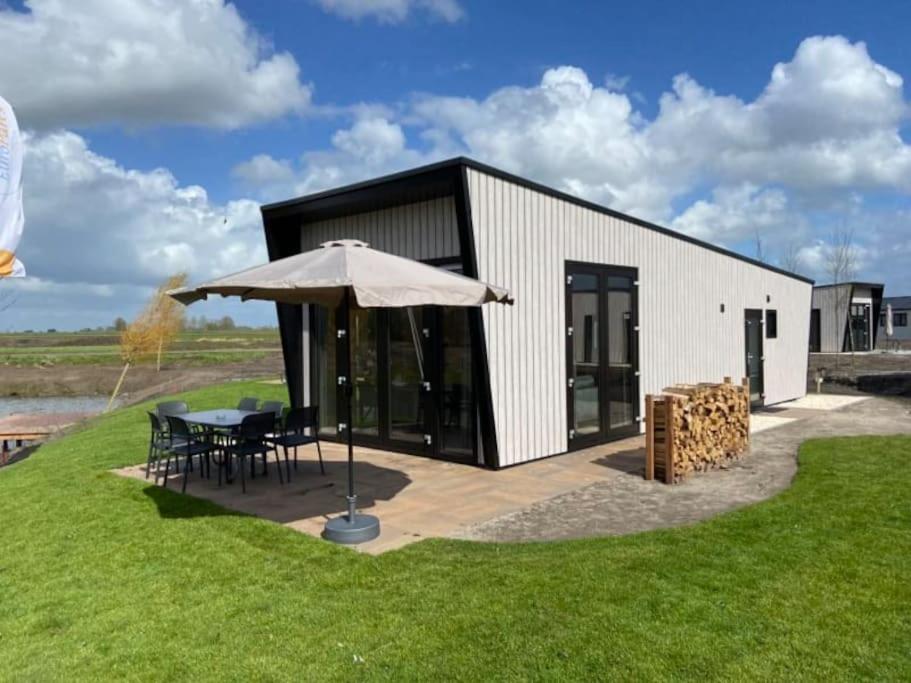 um edifício com uma mesa e um guarda-chuva em Tiny vakantiehuis aan het water met eigen steiger en airco em Kampen