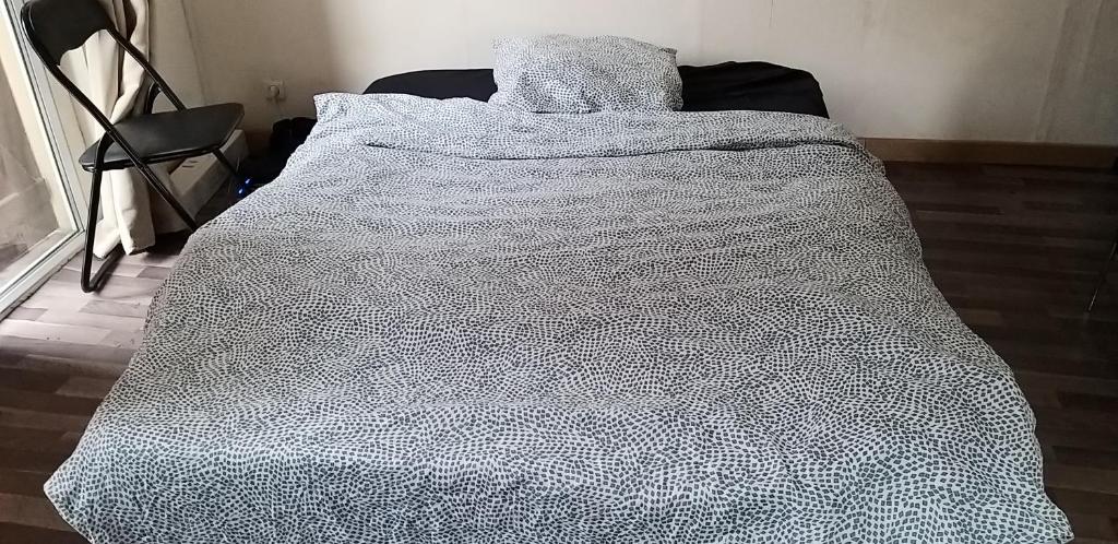 Una cama con una manta blanca y negra. en Chambre équipée (proche Paris), en Argenteuil