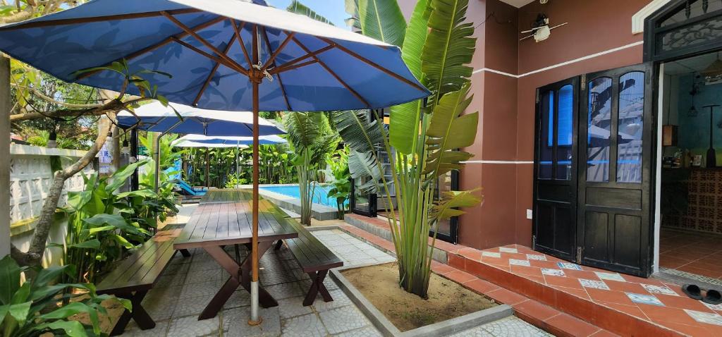 eine Terrasse mit einem Tisch und einem blauen Sonnenschirm in der Unterkunft An Bang Gold Coast Beach Villa in Hoi An