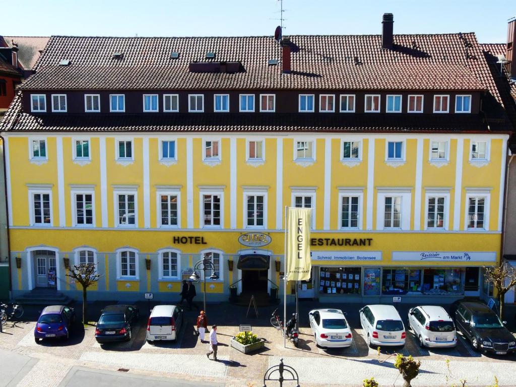 un grand bâtiment jaune avec des voitures garées dans un parking dans l'établissement Hotel Engel, à Langenargen