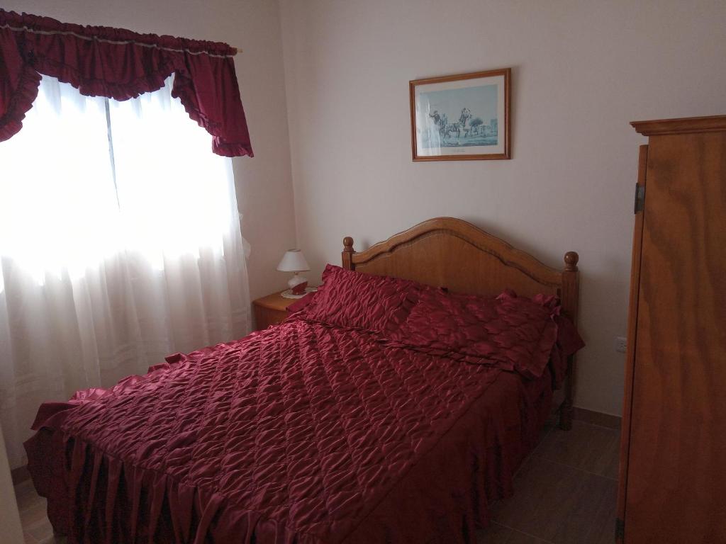 1 dormitorio con 1 cama con edredón rojo y ventana en Viajeros en Buenos Aires en Monte Grande