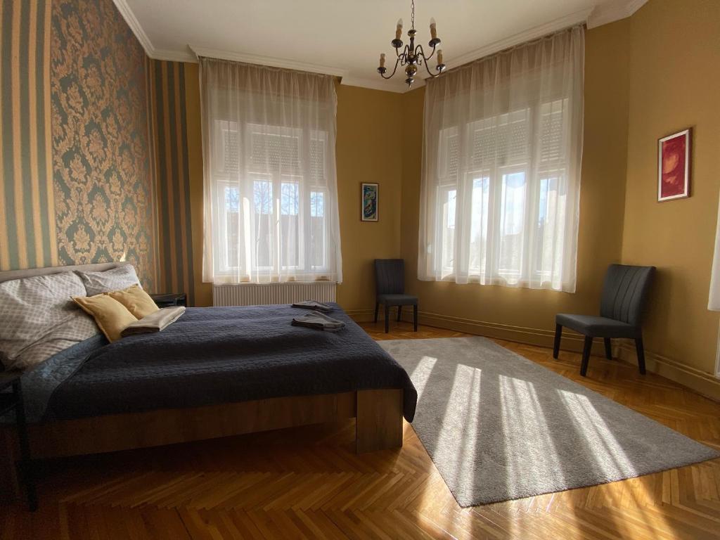 a bedroom with a bed and two chairs and windows at Ambrózia Apartman in Eger