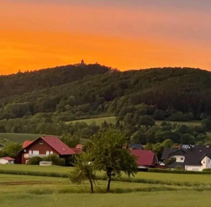 a house in a field with a sunset in the background at Ferienwohnung Leuchtbergblick mit Terrasse und PKW Stellplatz in Eschwege