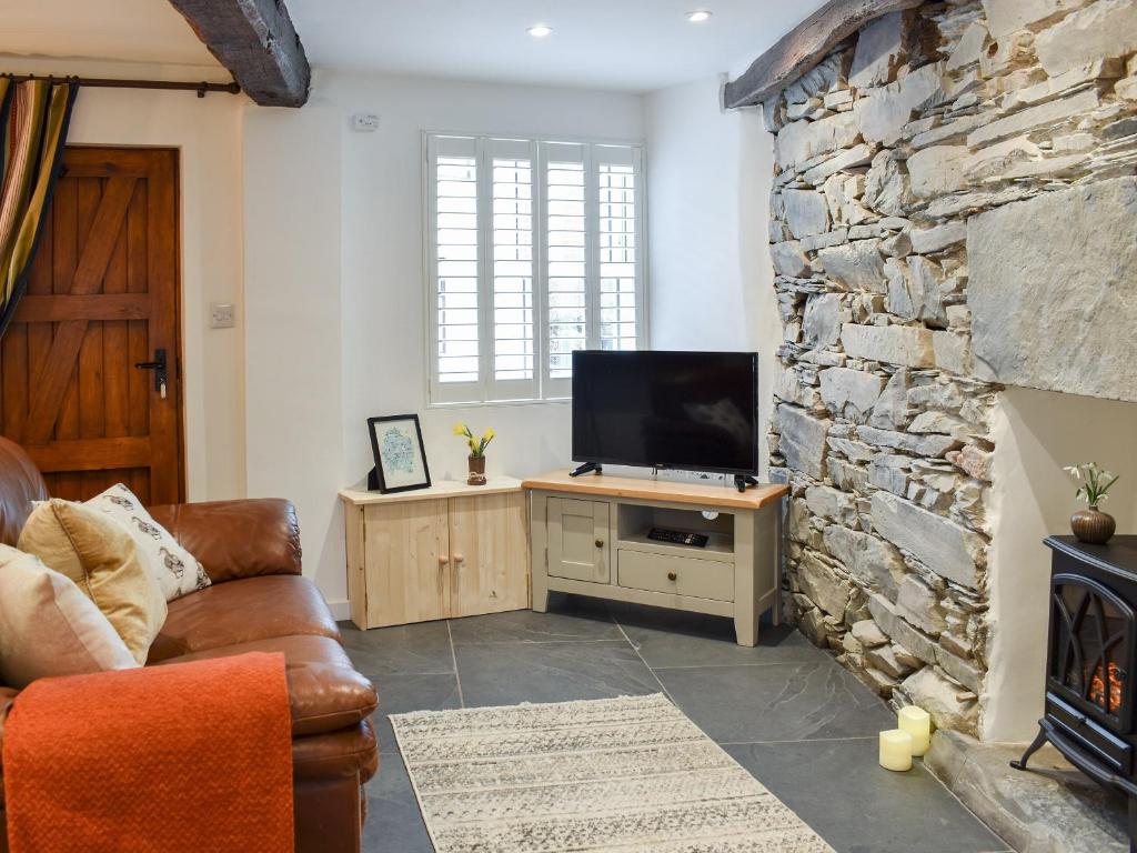 a living room with a tv and a stone wall at Ugly Duckling Cottage in Broughton in Furness