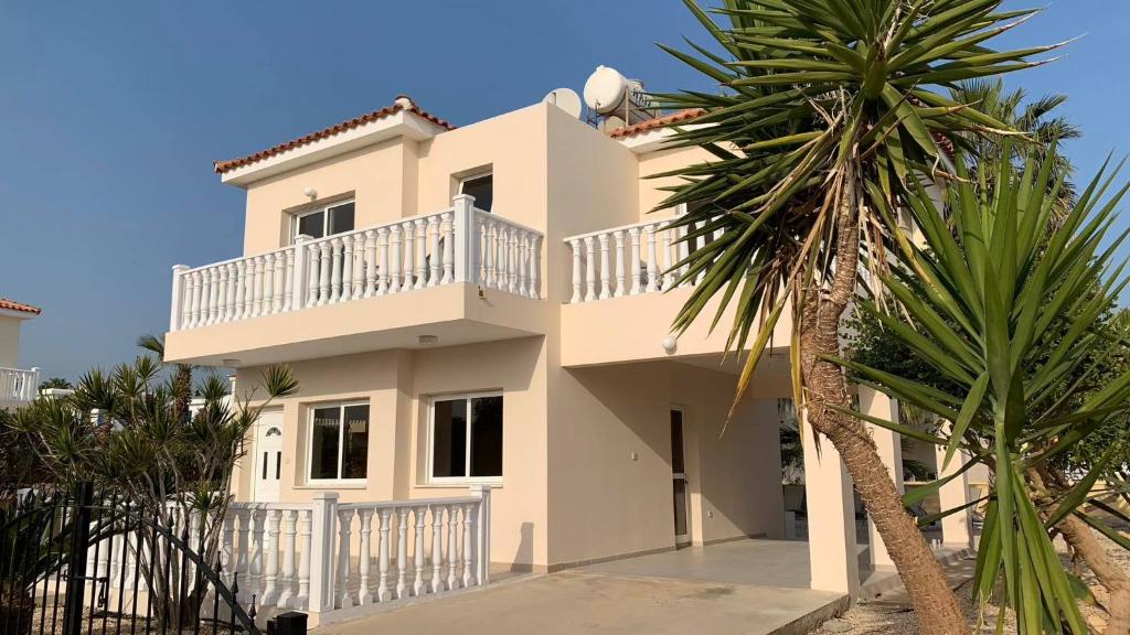 Cette maison blanche dispose d'un balcon et d'un palmier. dans l'établissement Sunset Sea View Villa, à Ayia Napa