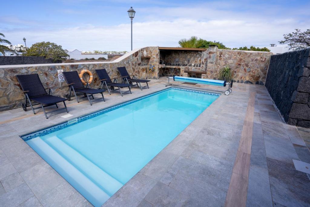 a swimming pool with chairs and a stone wall at Villa Piedra in Playa Blanca