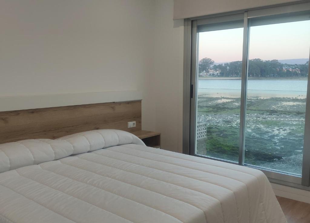 a bedroom with a white bed and a large window at Apartamentos O Grove Awa Bay in O Grove