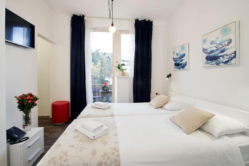 a white bedroom with two beds and a window at Art Like Rooms in Zagreb
