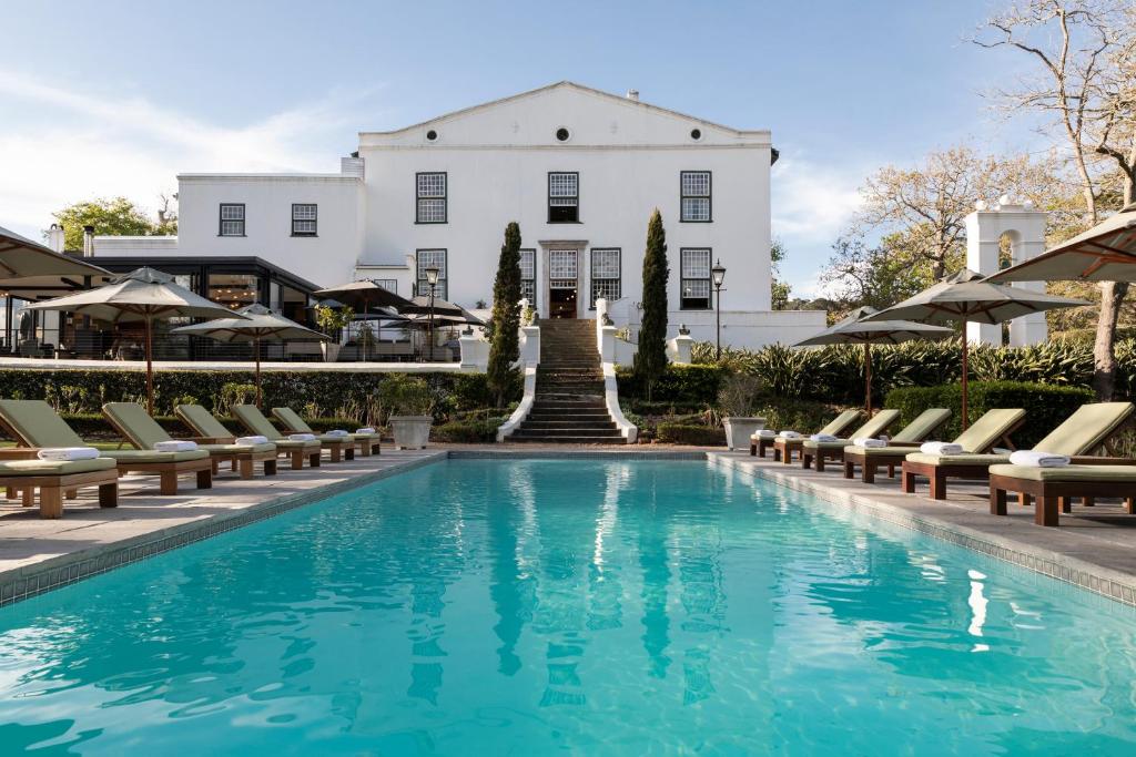 a pool in front of a white house with chairs and a building at The Alphen Boutique Hotel & Spa in Cape Town