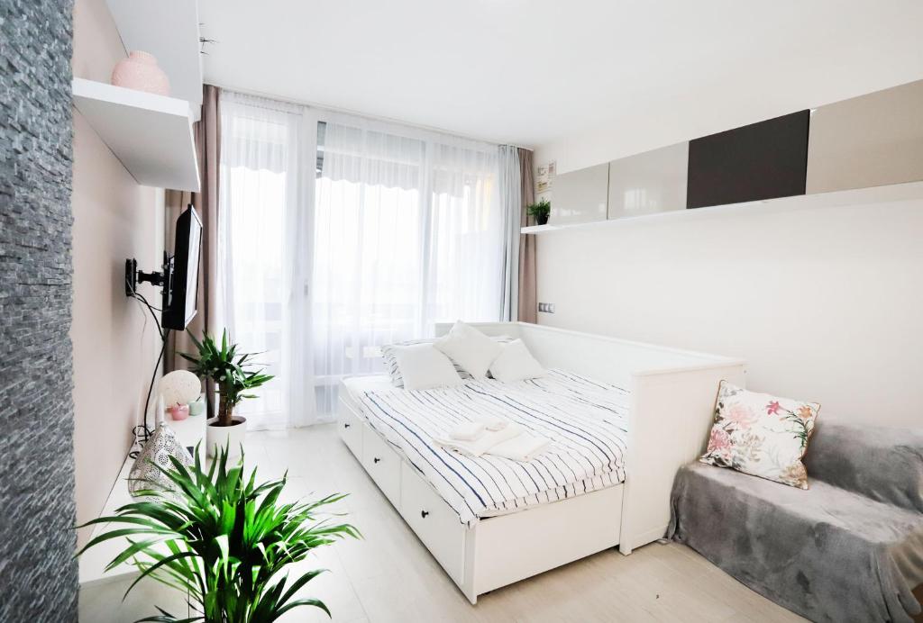 a small white bedroom with a bed and a window at Silver Lodge Ezüstpart Apartman in Siófok