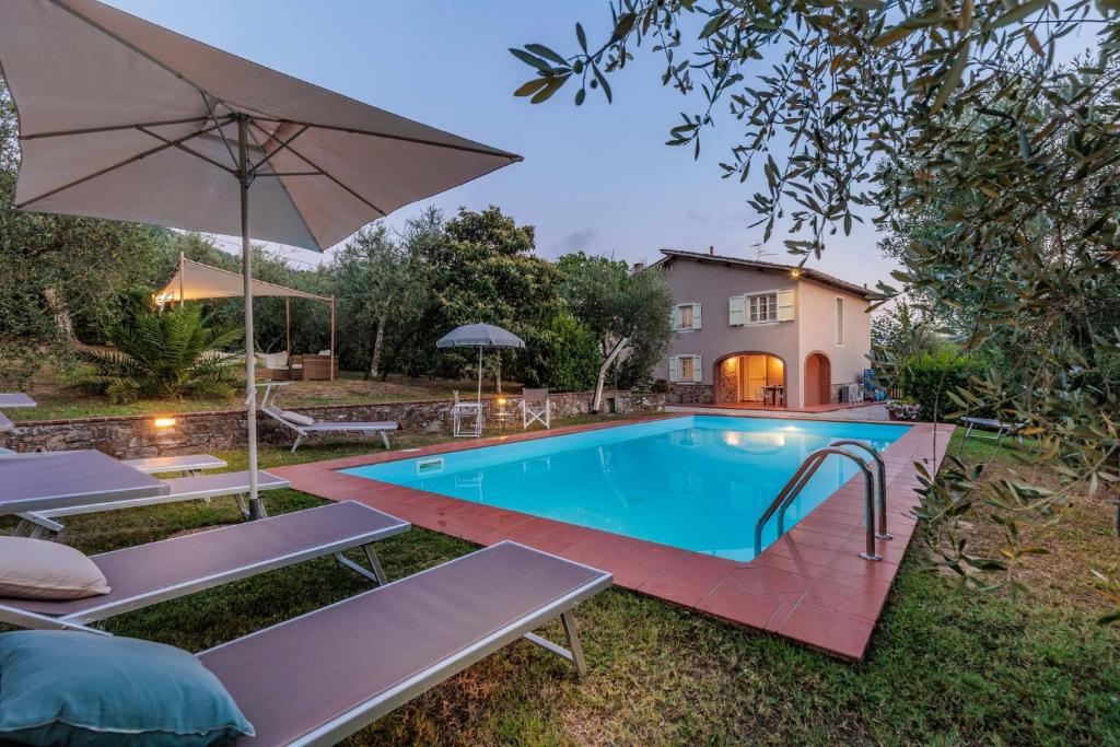 una piscina con sillas, una sombrilla y una casa en Villa Dondolino, a Stylish Farmhouse en Lucca