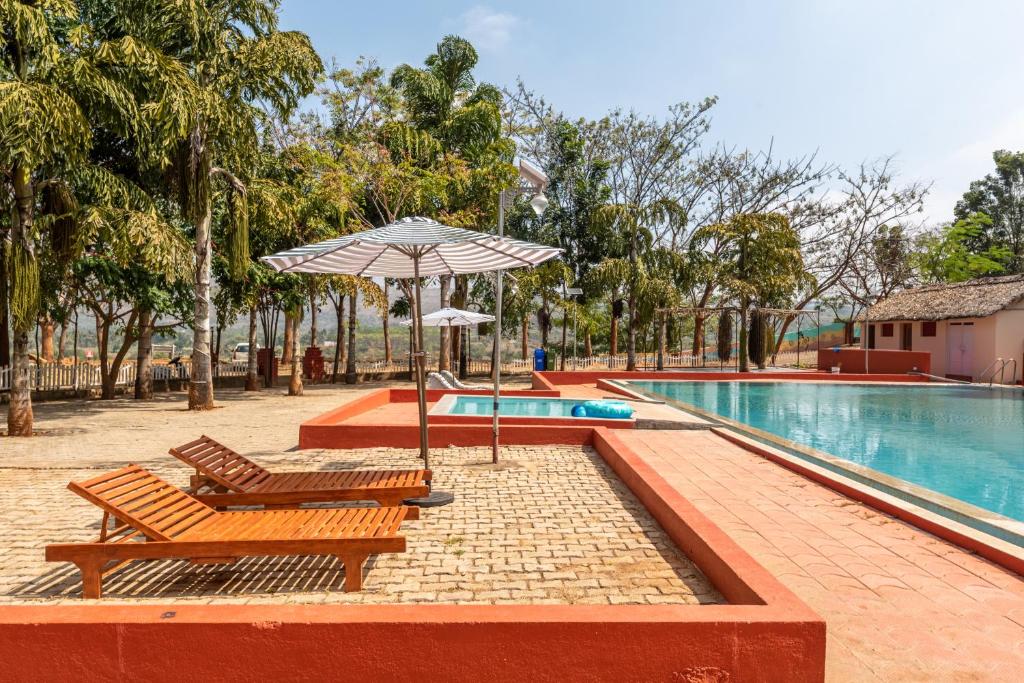 una piscina con 2 sillas y una sombrilla junto a una piscina en Anvesana I Yoga Spa Retreat, en Dod Ballāpur