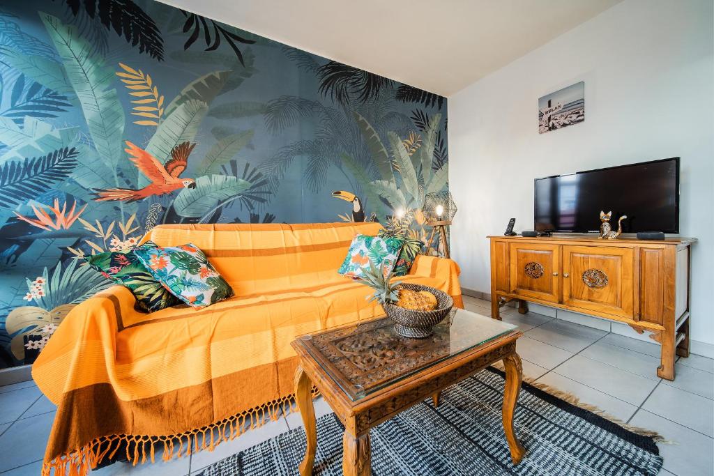 a living room with an orange couch and a tv at Ti case a moin - Joli T2 en bord de mer in Saint-Pierre