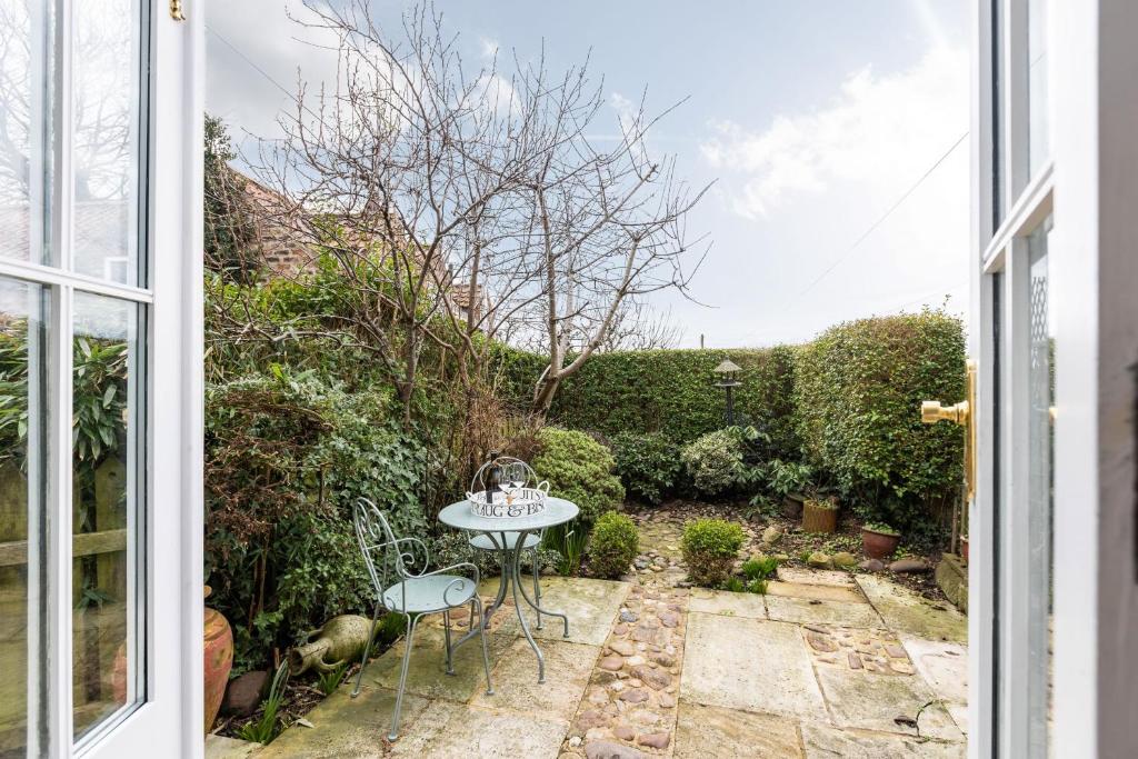 a patio with a table and chairs outside a window at Quaint Cottage in the heart of North Yorkshire Village - Pet Friendly FREE in Stillington