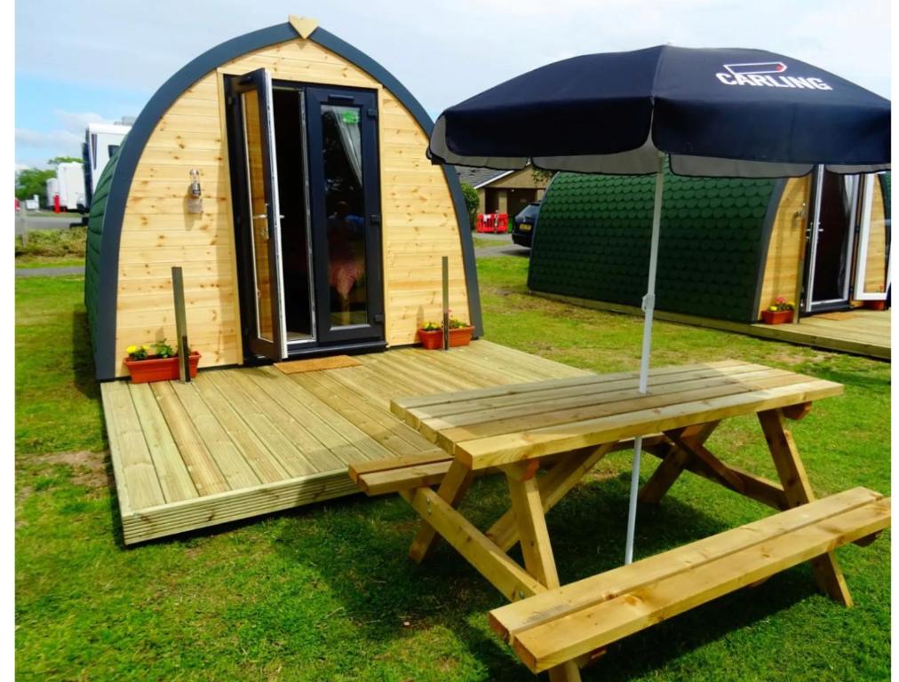 een houten terras met een picknicktafel en een parasol bij Gateway Glamping Pods in Llanelli