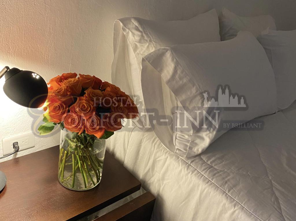 un jarrón de flores en una mesa junto a una cama en HOSTAL COMFORT- INN by BRILLIANT, en Quito