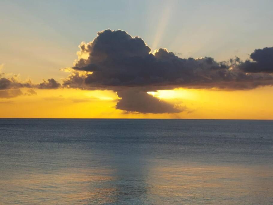 a sunset over the ocean with a cloud over the water at Superbe appartement vue mer - résidence de standing in Schœlcher