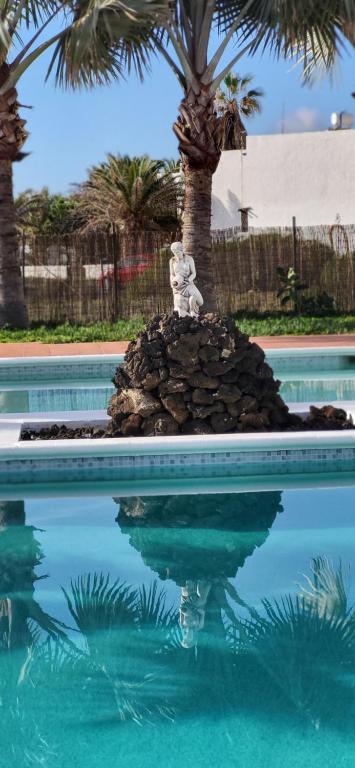 a statue in the middle of a pool with palm trees at Villa Harmony in Charco del Palo