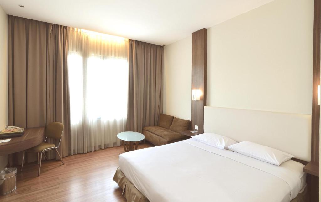 a hotel room with a white bed and a desk at Grand Cikarang Hotel in Tegalgede