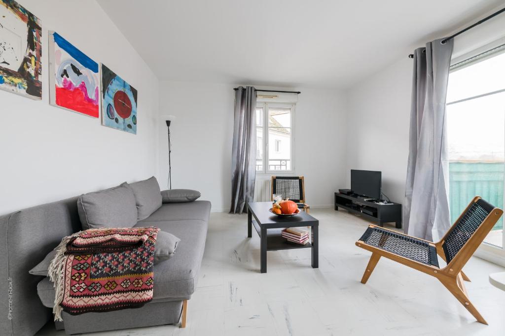 ein Wohnzimmer mit einem grauen Sofa und einem Tisch in der Unterkunft Les 2 Lys in Brétigny-sur-Orge