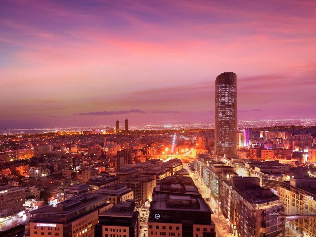 um horizonte da cidade à noite com um edifício alto em Amman Rotana em Amã