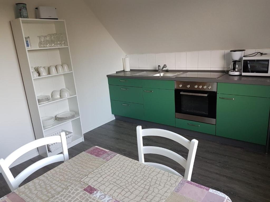 eine Küche mit grünen Schränken sowie einem Tisch und Stühlen in der Unterkunft NEU Ferienwohnung Kropp OG - Links in Kropp