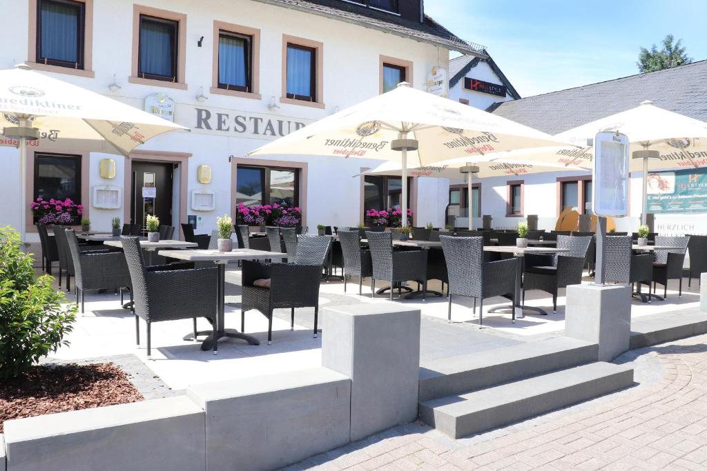 un restaurante con mesas, sillas y sombrillas en Hotel Restaurant Haus Zwicker en Bleialf