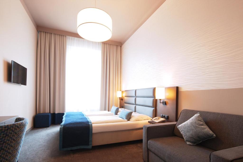 a bedroom with a bed and a couch and a window at Drei Kronen Hotel Wien City in Vienna