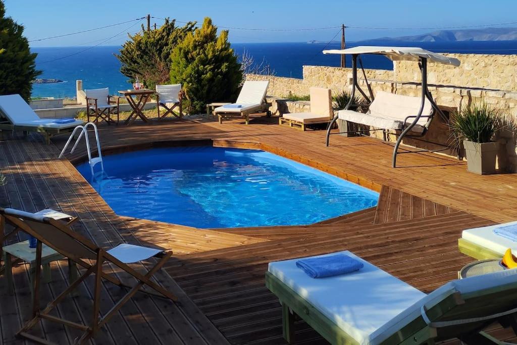 uma piscina num deque de madeira com cadeiras e um guarda-sol em Pamela's house "private pool and spa" em Karteros