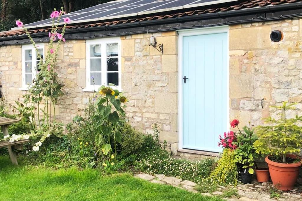 a stone house with a white door and some flowers at The Studio @ Cleeve Hill in Bath