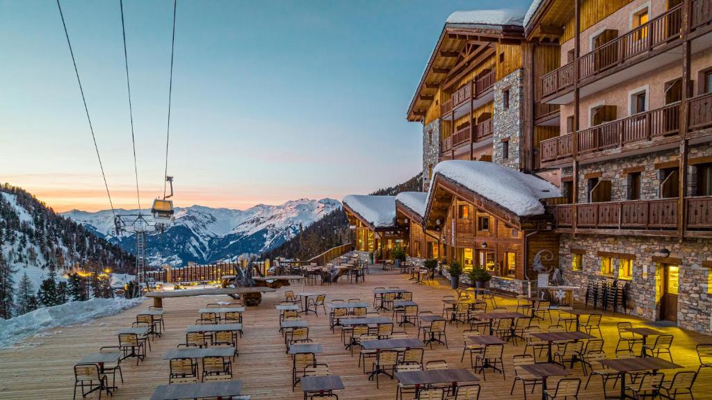 un groupe de tables et de chaises sur une terrasse avec des montagnes dans l'établissement Résidence Carlina by Les Etincelles, à Belle Plagne