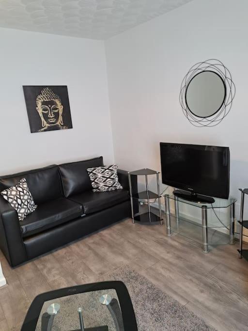 uma sala de estar com um sofá preto e uma televisão de ecrã plano em 1 Bed Apart em Dowlais