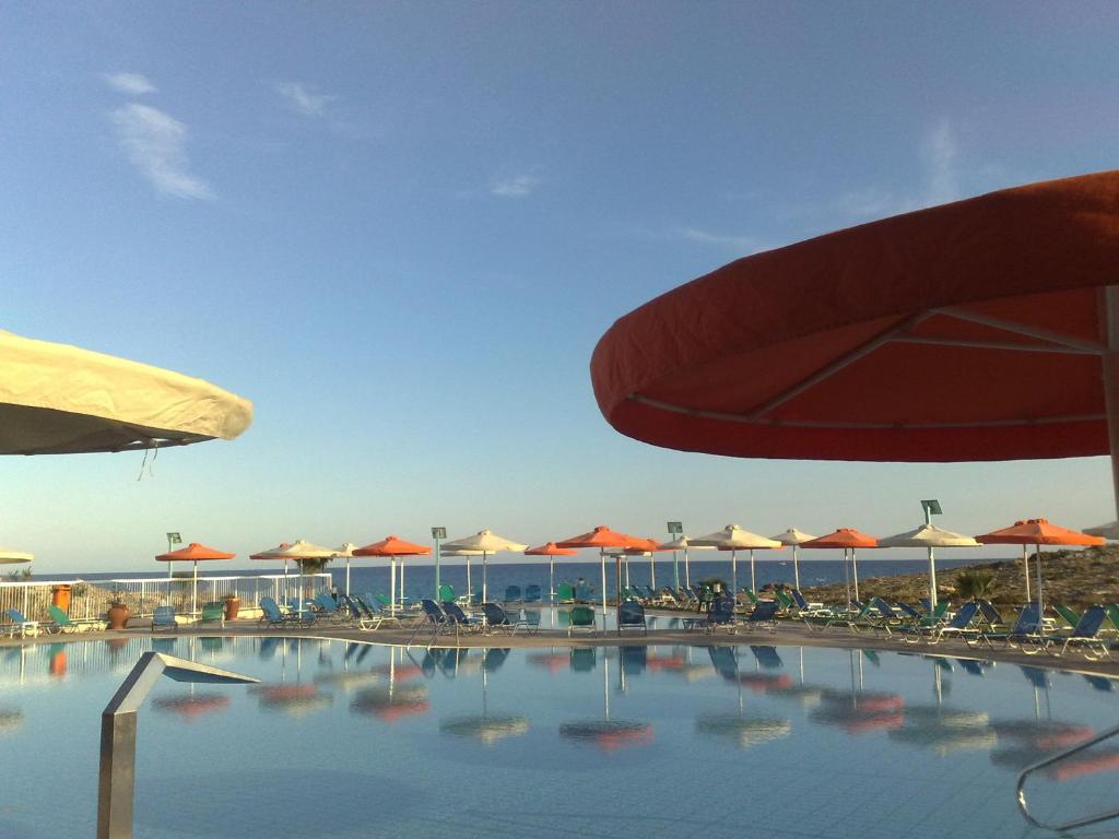 a swimming pool with chairs and umbrellas at Aktea Beach Village in Ayia Napa