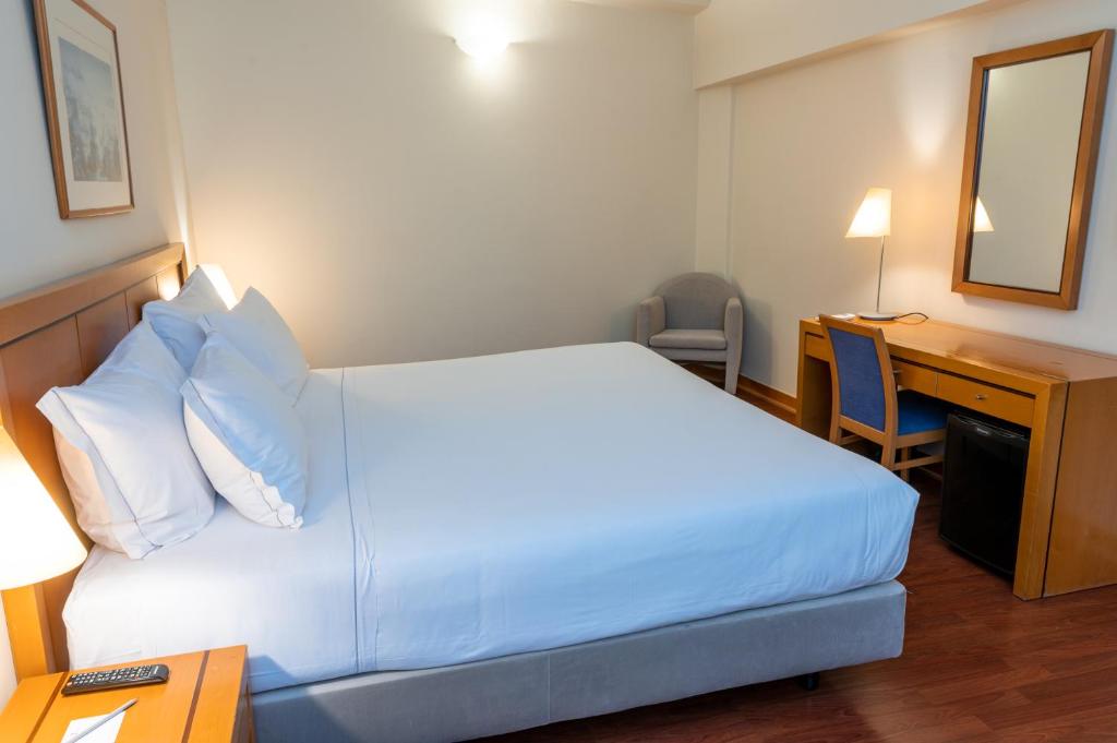 A bright hotel bedroom combines a large bed with a compact desk area.