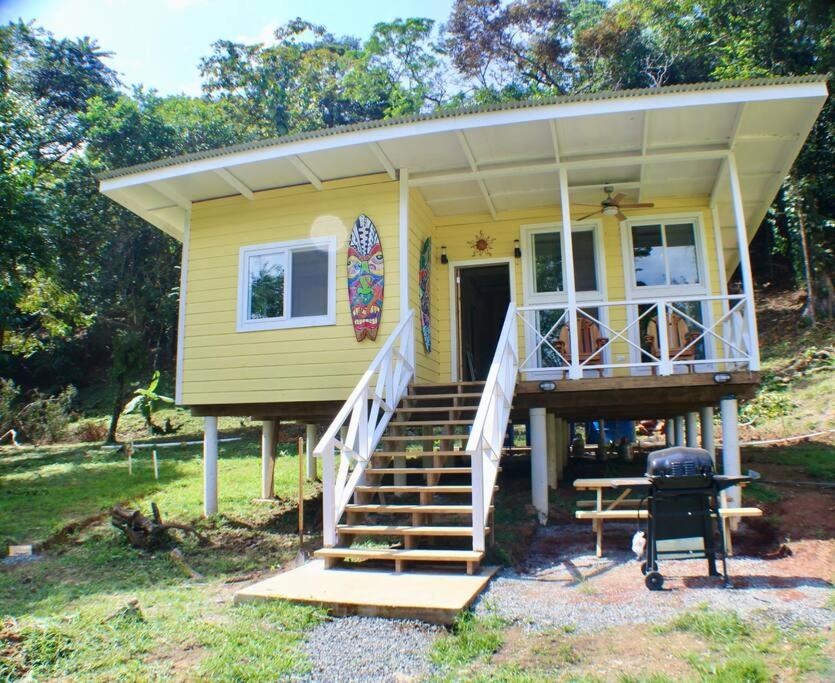 una pequeña casa amarilla con porche y parrilla en The Birds Nest, en Bocas Town